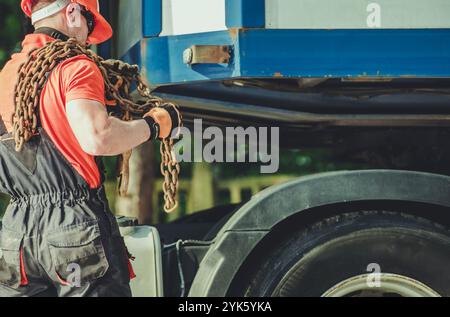 A worker in protective gear fastens a large cargo container to a vehicle using heavy chains, showcasing important loading procedures outdoors. Stock Photo