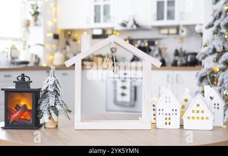 Key and tiny house of a small size on cozy home with Christmas decor on table of festive white kitchen. Gift for New Year. Insurance, moving to new ho Stock Photo