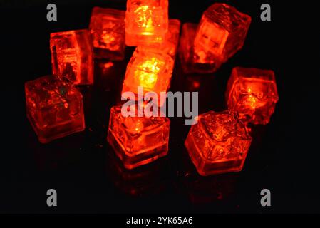 Red glowing ice cubes are located on a black glossy with water drops. Plastic things made in the form of ice cubes with a built-in diode illuminate. Stock Photo