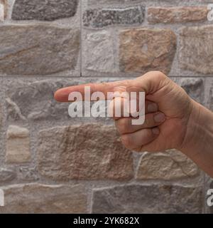 Hand pointing directly with one finger against a textured stone wall background Stock Photo