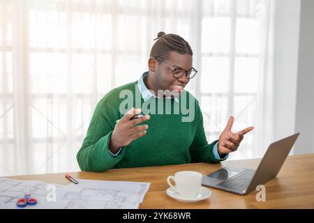 Engaged young man in green sweater participating in a virtual meeting at home Stock Photo