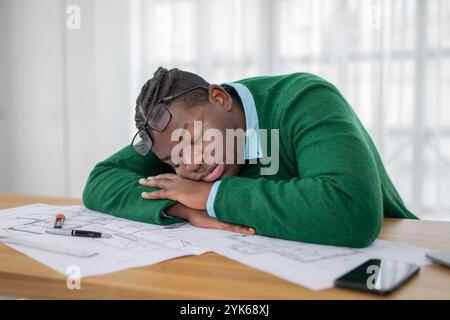 Young man sleeping at desk surrounded by design drafts in a bright office Stock Photo