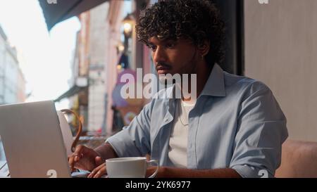 Serious man customer visitor client tourist traveler drink coffee urban cafe outdoors Indian Arabian guy booking hotel online order shopping male Stock Photo