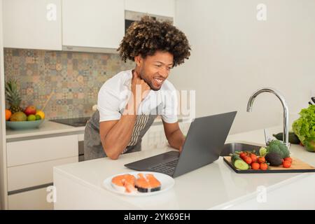 Young man prepares sushi while using laptop in modern kitchen Stock Photo