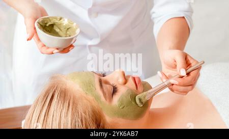 Facial and beauty. Beautician smears client face with clay Stock Photo