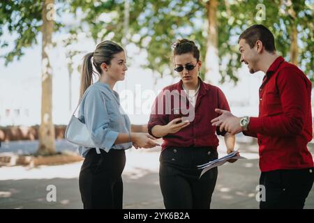 Business meeting outdoors with three colleagues discussing work and using a smart phone Stock Photo