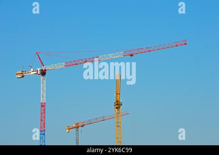 Three multi-colored tower cranes against a cloudless sky Stock Photo