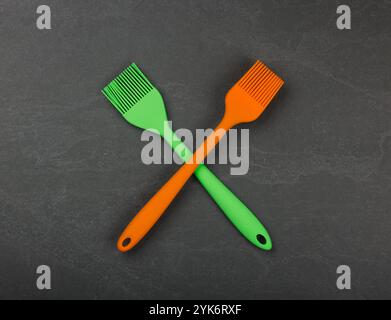 Two silicone brushes for pastry or basting on black slate board with copy space, colorful modern culinary kitchen utensils, close up, elevated table t Stock Photo