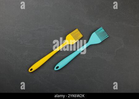 Two silicone brushes for pastry or basting on black slate board with copy space, colorful modern culinary kitchen utensils, close up, elevated table t Stock Photo
