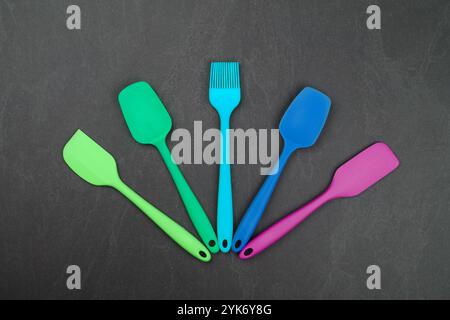 Five silicone cooking spatulas and brushes on black slate board with copy space, colorful modern culinary kitchen utensils, close up, elevated table t Stock Photo