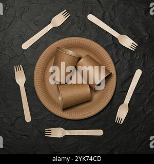 Close up disposable brown paper plates, takeaway coffee cups and wooden forks on black background, natural eating and drinking utensils, close up, ele Stock Photo