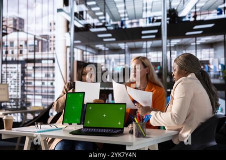 Multicultural team of specialists using mockup copy space in the office, working with resilience to accomplish enterprise objectives. Manager and employees meeting for a briefing. Stock Photo