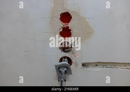 Electric wiring installation in progress with exposed wires, wall-mounted electrical boxes, and a partially plastered wall during renovation Stock Photo