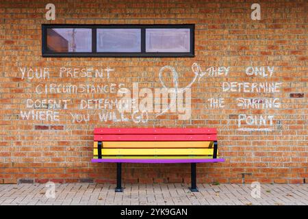 Motivational words written in chalk on a brick wall with a rainbow bench in front. Stock Photo