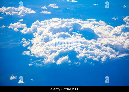 Large formation of fluffy white clouds viewed from above, likely from an airplane or satellite. Clouds casting shadows on the landscape below, creatin Stock Photo