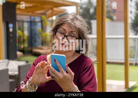 Portrait of a senior woman with glasses using her cell phone outdoors in the morning Stock Photo