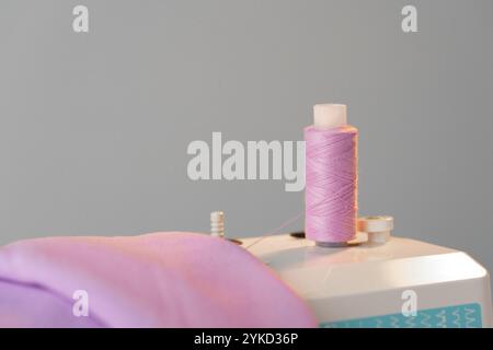 View of a sewing machine with a spool of pink thread placed on top Stock Photo
