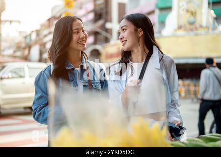 Two cheerful, cute Asian female tourists buy street food in Thailand, enjoying a summer stroll through Chinatown, traveling in Southeast Asia. food st Stock Photo