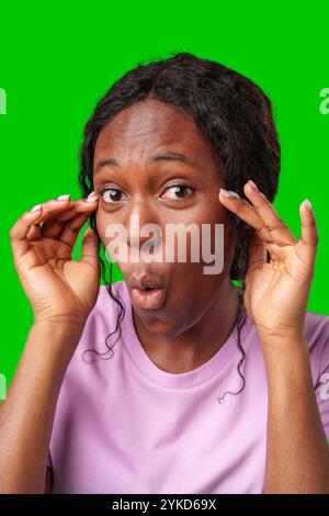 Surprised woman expressing shock while posing with hands on her face against a bright green backdrop Stock Photo