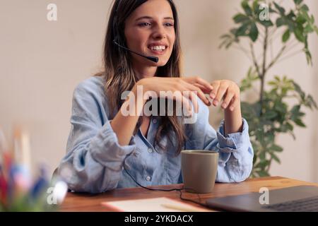 Happy female professional sharing ideas during virtual team meeting while enjoying coffee break in contemporary home office environment Stock Photo