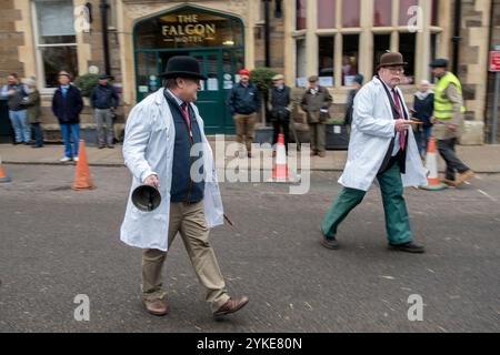 Livestock auctioneer wearing traditional white smock coat and black Bowler hat, his assistant in a Brown Bowler Derby hat. Ringing the bell to start the annual Christmas Fatstock Market auction that takes place annually in November. The Market Square at Uppingham, Rutland England 24th November 2021 2020s HOMER SYKES Stock Photo