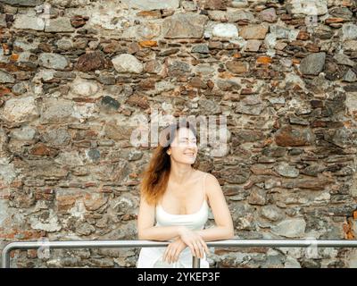 Smiling woman leaning on railing in front of a stone wall Stock Photo