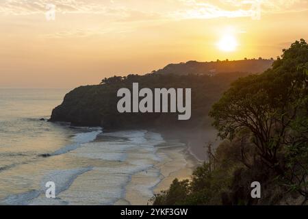 A breathtaking view of the sun setting over the Pacific Ocean at Mizata Beach, El Salvador, highlighting the coastline and lush foliage Stock Photo