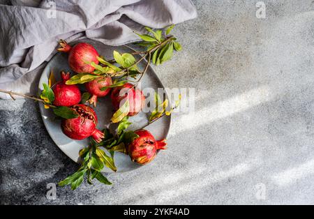 Top view of a cluster of ripe pomegranates, some sliced open, arranged on a gray stoneware plate next to a draped gray cloth, set against a textured g Stock Photo