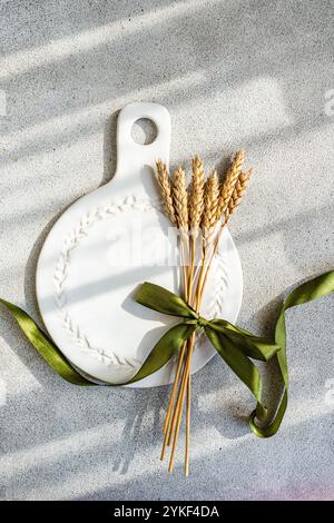 A sophisticated table setting featuring a white decorative ceramic platter adorned with a bundle of wheat tied with a green ribbon Perfect for rustic Stock Photo