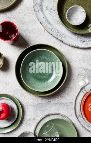 Top view of a collection of artisan ceramic tableware including plates, bowls, and glasses arranged on a textured grey surface. The image showcases a Stock Photo