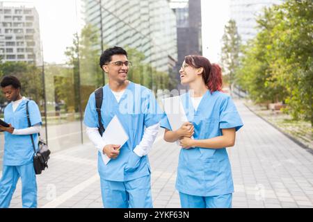Two cheerful nursing students walk and engage in conversation in an urban university campus, displaying a relaxed yet professional demeanor Stock Photo