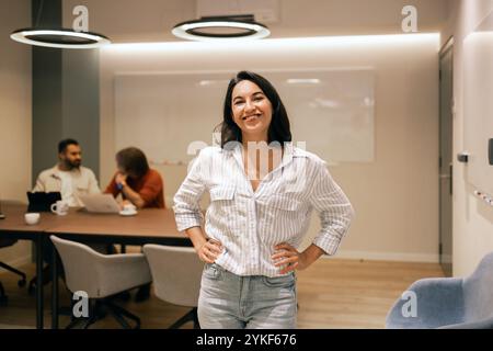 A cheerful professional stands confidently in a bright, modern coworking space Colleagues collaborate in the background, creating a dynamic and produc Stock Photo