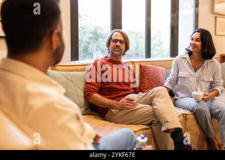 A diverse group of professionals engaged in a lively conversation, seated comfortably with coffee mugs in hand The scene captures a creative and colla Stock Photo