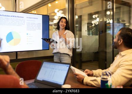 A woman gives an engaging presentation on AI in a modern coworking space Team members actively listen and discuss, creating a collaborative and dynami Stock Photo