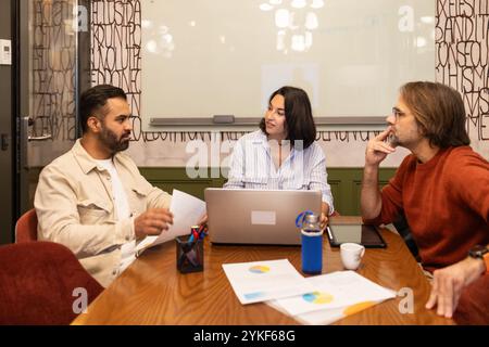 A diverse group of professionals engaged in a meeting in a modern coworking space They are collaborating over laptops, papers, and coffee in a creativ Stock Photo