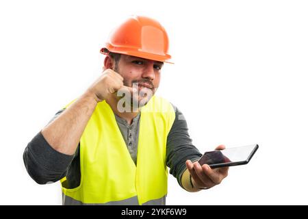 Friendly cheerful construction man holding phone making call me gesture using fingers wearing work equipment hardhat and vest isolated on white studio Stock Photo