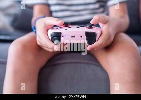 Close up of a child's hands holding a pink game controller focused on playing a video game, showcasing modern childhood interaction with technology Stock Photo