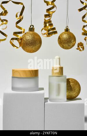 A festive arrangement of gold colored Christmas baubles intertwined with golden streamers, complemented by elegant cosmetic products on display pedest Stock Photo