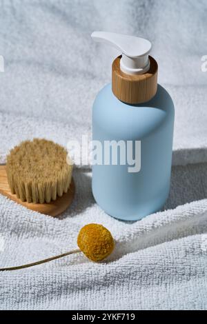 A stylish blue SPA cosmetic bottle with wooden cap pump, accompanied by a natural brush and a dried flower on a white textured towel, perfect for well Stock Photo