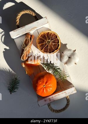 Top view of a wooden tray filled with fresh mandarins, dried orange slices, and seasonal decorations, bathed in soft sunlight creating a cozy atmosphe Stock Photo