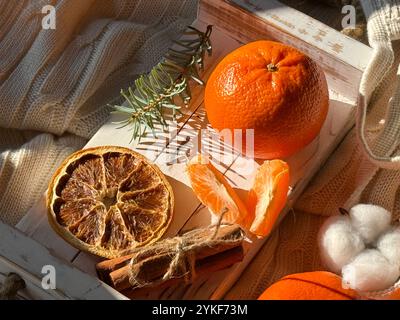 From above, a cozy and inviting scene with fresh mandarins on a textured knit background, accompanied by dried orange slices and soft cotton bolls. Stock Photo