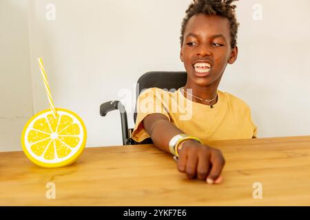 A young African american boy in a wheelchair with cerebral palsy is pictured engaging happily with activities at his holiday home, supported by modern Stock Photo