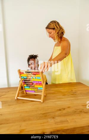 An African American boy with curly hair and his female teacher using an abacus at a holiday home. The child, with cerebral palsy, is concentrating on Stock Photo