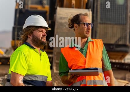Two safety inspectors, each wearing reflective vests and hard hats, evaluating safety protocols at a construction site for renewable energy infrastruc Stock Photo