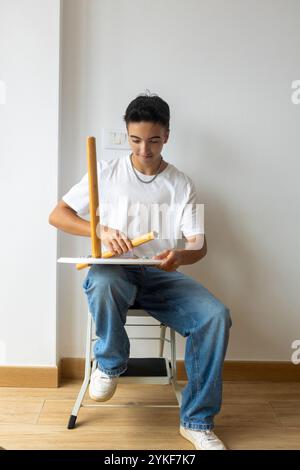 A smiling trans man assembles a wooden chair in his new apartment, symbolizing a fresh start and self-reliance within the LGBTQIA+ community Stock Photo