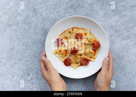 A dish of ravioli stuffed with goat cheese and caramelized onion presented in a white plate, topped with tomato sauce and candied cherry tomatoes, hel Stock Photo