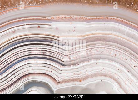 Close-up of a stunning Laguna Lace agate showcasing its intricate banding patterns in creamy white, beige, and rust tones Tiny red specks add vibrant Stock Photo