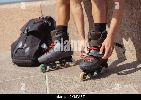 Cropped unrecognizable young male rollerblader securing laces on his inline skates on a sunny day, close-up of hands and skates. Stock Photo
