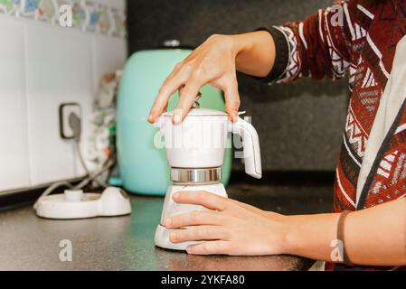 Cropped unrecognizable woman using a moka pot to make coffee in a cozy home kitchen, highlighting a daily morning routine. Stock Photo