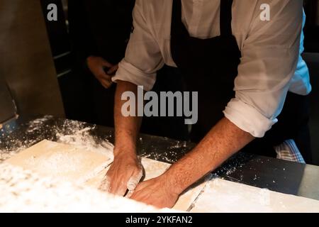 Two chefs are intensively working together in a bustling restaurant kitchen, skillfully preparing dough on a floured surface Stock Photo